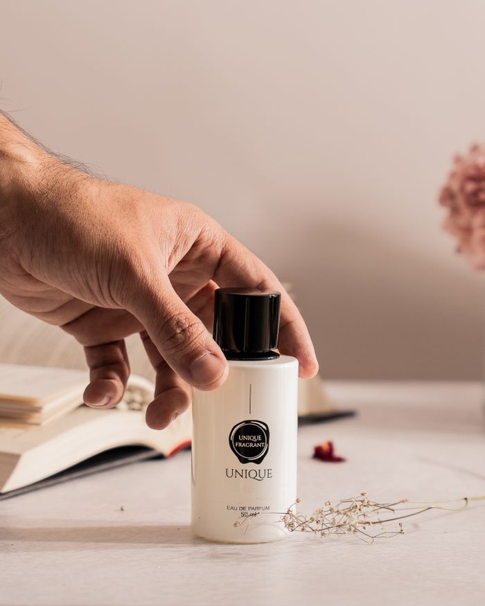 Hand reaching for a perfume bottle with books and flowers on a well-lit desk setting.